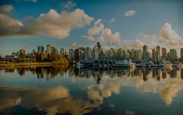 City skyline with buildings and boats reflected in water, blue sky with clouds