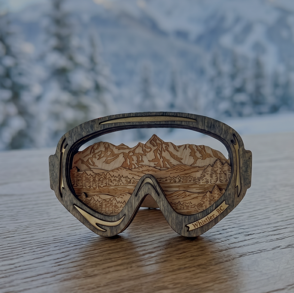Wooden goggles with mountain design on a wooden surface with a snowy landscape background