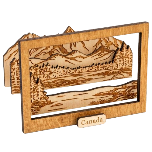 A wooden laser-cut landscape plaque featuring mountains, trees, and a river, with a small front label reading Canada, shown on a plain white background.